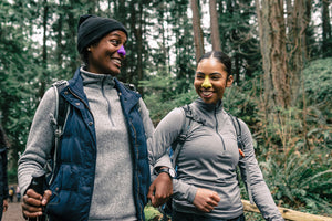 Two women walking through a green forest, they are wearing Noz sustainable and earth friendly sunscreen which comes in 4 unique colors